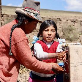 Photo of a woman and a girl getting water from an outdoor fountain